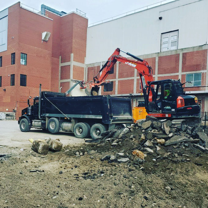 An excavator dumping rubble into a dump truck.